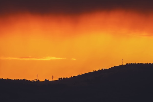 Paisagem atmosférica com silhueta escura de montanha com árvores no fundo do céu laranja vívido do amanhecer. Cenário colorido da natureza com pôr do sol ou nascer do sol de cores iluminadoras. Vívido pagamento do pôr-do-sol.