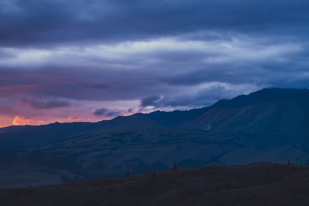 Paisagem atmosférica com silhuetas de montanhas no fundo do céu vívido do amanhecer. Cenário colorido da natureza com pôr do sol ou nascer do sol de laranja azul magenta violeta rosa lilás cor. Salário de Sundown.