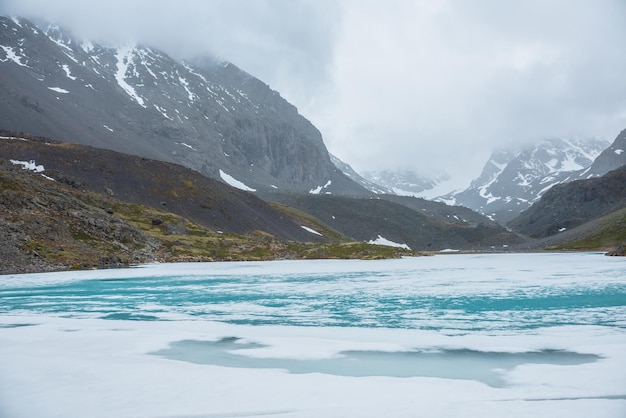 Paisagem atmosférica de montanha com lago alpino congelado e altas montanhas nevadas Impressionante cenário nublado com lago de montanha gelado no fundo de montanhas de neve em nuvens baixas Vista panorâmica para o lago de gelo