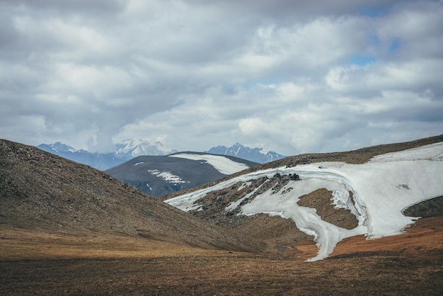 Paisagem cênica das terras altas com uma pequena geleira no alto das montanhas nas colinas no fundo do pico de alta montanha nevada. Impressionante paisagem montanhosa com grandes montanhas nevadas sob a luz do sol e céu nublado