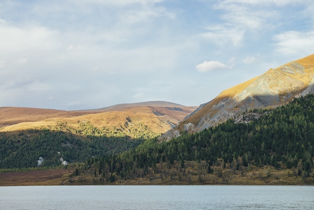 Paisagem cênica de outono com lago de montanha e montanhas heterogêneas com floresta. Vista alpina colorida para lago raso e grandes colinas multicoloridas em cores de outono. Belas paisagens montanhosas vivas no outono.