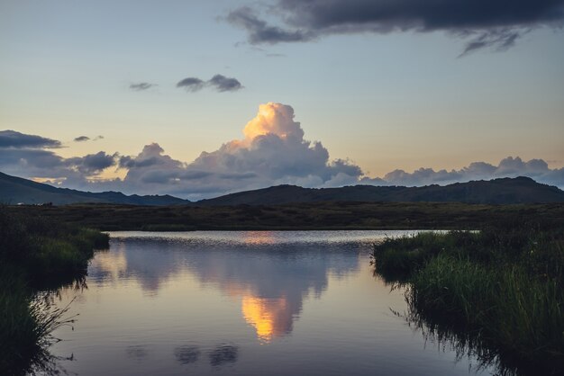 Paisagem cênica do sol com grande nuvem amarela em forma de explosão acima do lago de montanha.