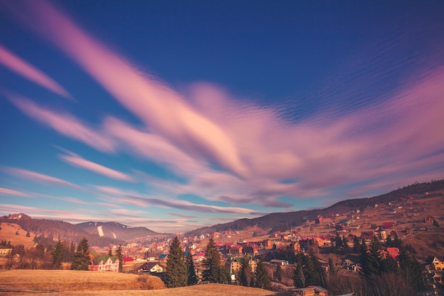 Paisagem colorida de outono no céu dramático e pitoresco da vila da montanha com nuvens cor de rosa