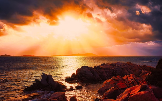 Paisagem com pôr do sol romântico na praia de Capriccioli na Costa Smeralda do mar Mediterrâneo na ilha da Sardenha, na Itália. Céu com nuvens. Província de Porto Cervo e Olbia. Mídia mista.