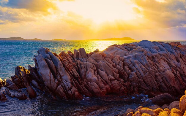 Paisagem com pôr do sol romântico na praia de Capriccioli na Costa Smeralda do mar Mediterrâneo na ilha da Sardenha, na Itália. Céu com nuvens. Província de Porto Cervo e Olbia. Mídia mista.