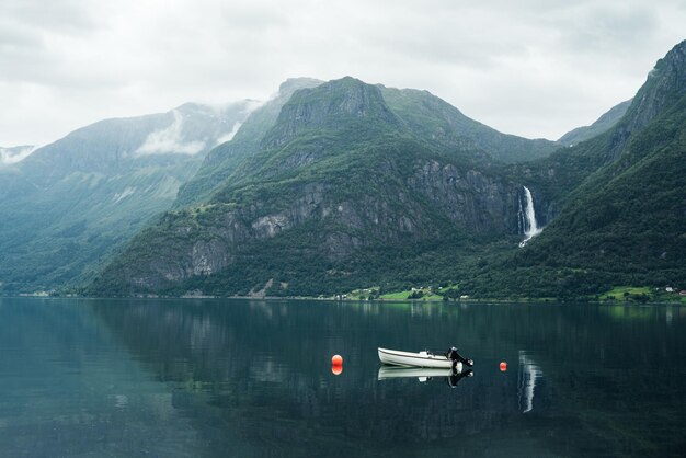 Paisagem com um barco no fiorde e uma cachoeira nas montanhas da Noruega