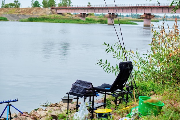 Paisagem com uma cadeira de pesca e uma vara de pescar na margem do lago pescando como hobby em seu tempo livre