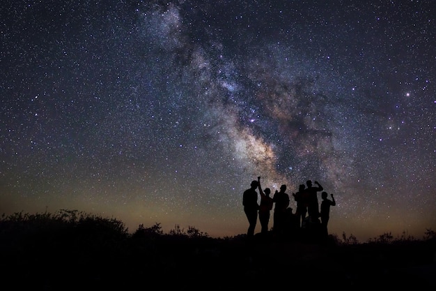 Paisagem com via láctea Céu noturno com estrela e silhueta de pessoas felizes em pé na montanha