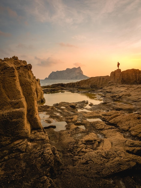 Paisagem costeira natural com piscinas naturais e a rocha Iffaz ao fundo ao pôr do sol