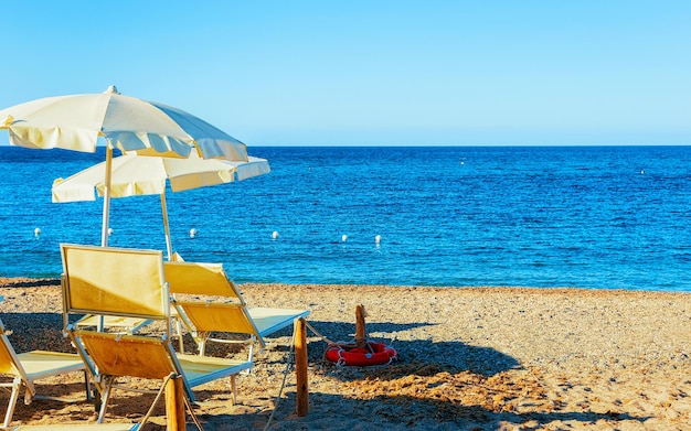 Paisagem da praia de Chia com guarda-chuvas e águas azuis do mar Mediterrâneo, na província de Cagliari, no sul da Sardenha, na Itália. Cenário e natureza. Mídia mista.