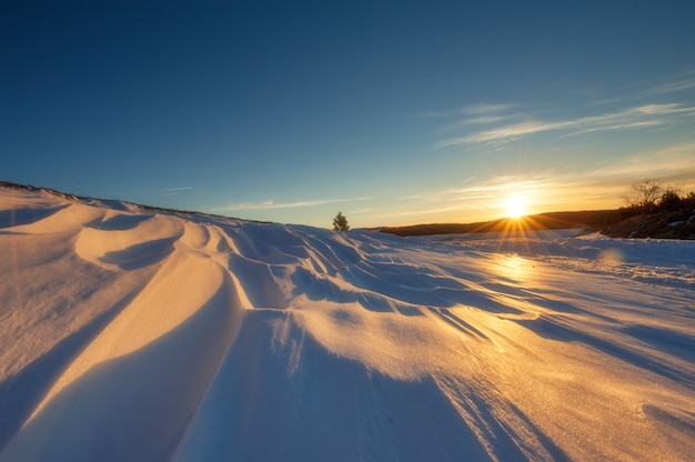 Paisagem de inverno, campos cobertos de neve e estradas em raios de sol no pôr do sol