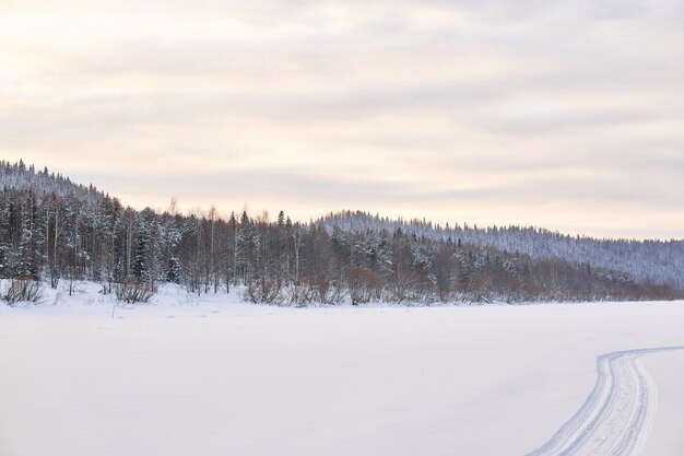 Paisagem de inverno com rio congelado em um vale nevado e arborizado com vestígios de um snowmobile na neve