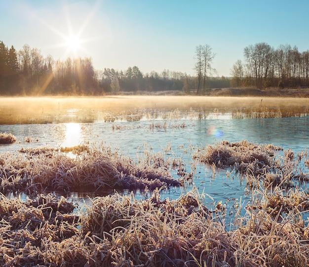 Paisagem de inverno com uma natureza fumegante no lago de gelo coberto de geada nos raios solares da manhã