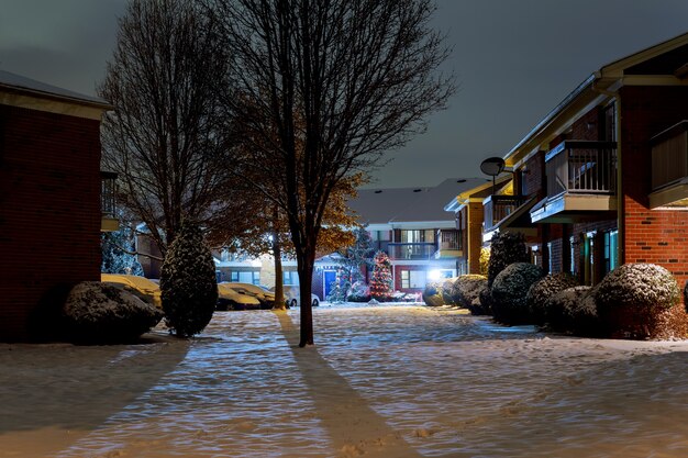 Paisagem de inverno noite - banco sob as árvores de inverno e luzes da rua brilhando com flocos de neve caindo