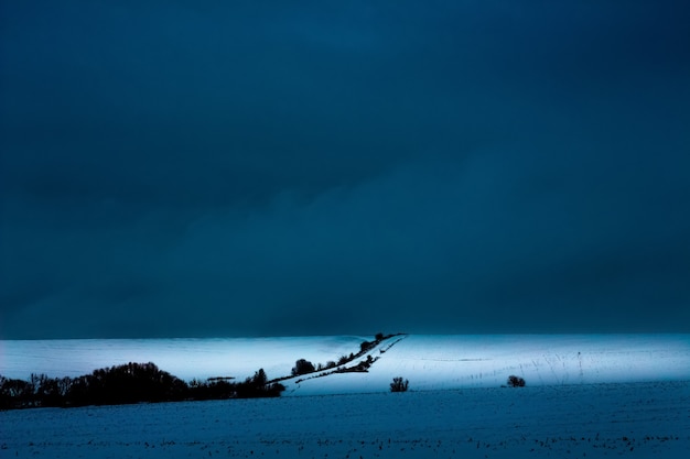 Paisagem de inverno, plano de fundo para a criatividade. a estrada fica no meio do campo no inverno, o céu escuro e tempestuoso_