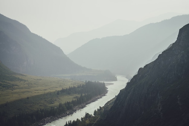 Paisagem de montanha enevoada com rio de montanha larga. Cenário sombrio verde escuro com confluência de dois rios de montanha na névoa. Vista atmosférica escura para a confluência de grandes rios em tempo chuvoso.