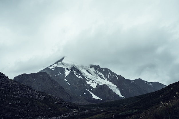 Paisagem de montanhas atmosféricas monocromáticas minimalistas com o topo de uma grande montanha de neve em nuvens baixas. Cenário mínimo impressionante com geleira nas rochas. Pináculo de alta montanha preto branco com neve nas nuvens.