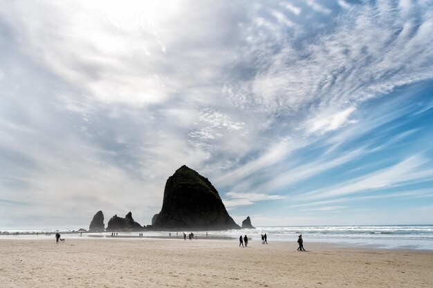 Paisagem de praia de canhão, oregon eua. paisagem nublada. férias de verão. pessoas andando na praia com água do mar ou oceano. natureza marinha.