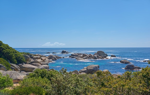 Paisagem de rochas no oceano em um dia quente de verão em Hout Bay Cape Town Ondas calmas espirrando contra o litoral rochoso e arbustivo Belas grandes rochas costeiras à beira-mar com vegetação exuberante