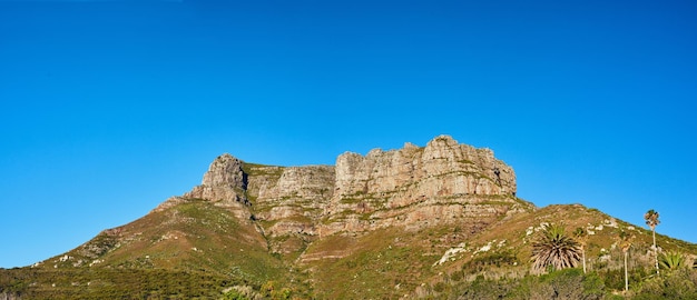 Paisagem de um pico de montanha na Cidade do Cabo, África do Sul Montanha acidentada com arbustos verdes, árvores de grama e um céu azul Uma atração turística popular e trilha de caminhada de aventura perto da montanha da mesa