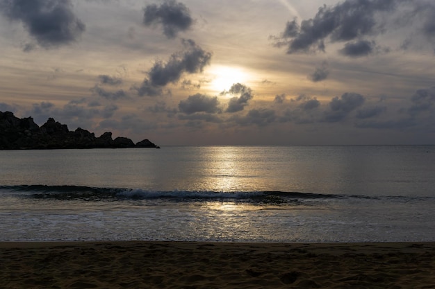 Paisagem de um pôr do sol na praia com a silhueta de algumas rochas