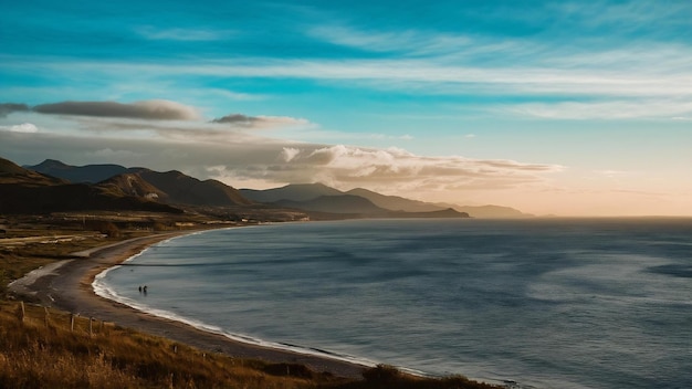 Paisagem de uma costa cercada por montanhas e mar sob um céu azul durante o pôr do sol