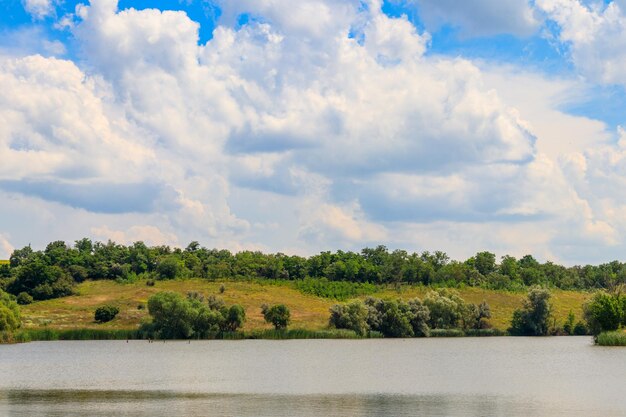 Paisagem de verão com belo lago, prados verdes, colinas, árvores e céu azul