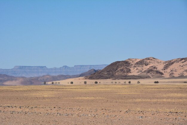 Paisagem desértica com uma colina distante à distância e areia seca em primeiro plano