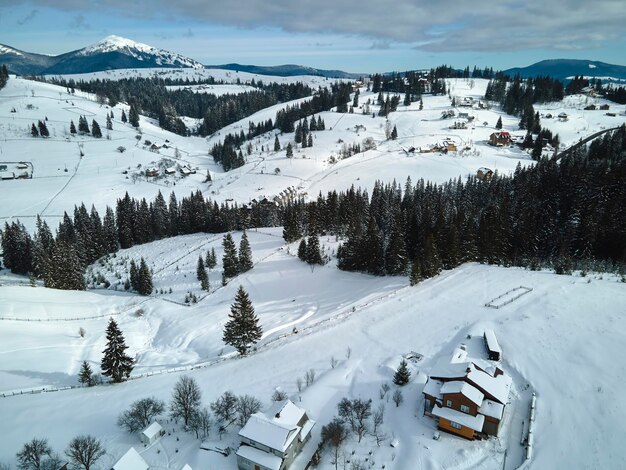 Paisagem do inverno com pequenas casas de aldeia entre a floresta coberta de neve em montanhas frias