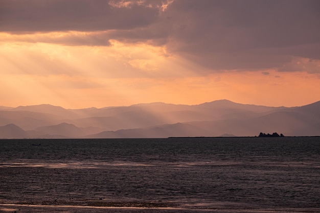 Paisagem do mar cercada por colinas sob um céu nublado e luz do sol durante um belo pôr do sol