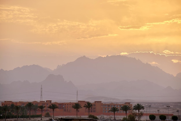 Paisagem do pôr do sol com complexo hoteleiro remoto contra picos de montanhas escuras no deserto egípcio