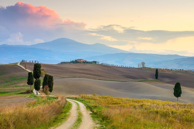 Paisagem do pôr do sol com estrada de terra em colinas fantásticas do campo e nuvens coloridas Toscana Itália Europa