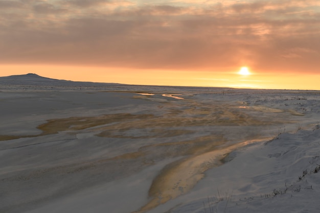 Paisagem do Ártico no inverno. Pequeno rio com gelo na tundra. Pôr do sol.