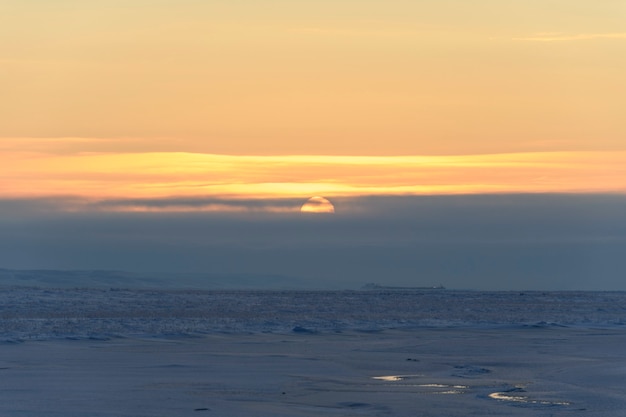 Paisagem do Ártico no inverno. Pequeno rio com gelo na tundra. Pôr do sol.