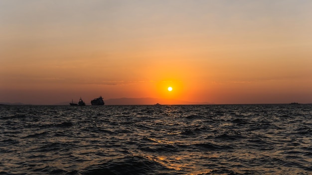 Paisagem do sol com o reflexo do sol na água do mar a silhueta de navios navegando e as montanhas ao fundo no porto de Izmir Turquia