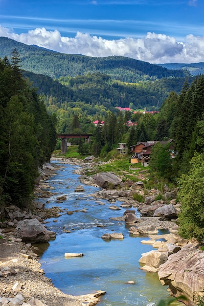 Paisagem dos cárpatos, montanhas, árvores, rio e ponte contra o céu azul