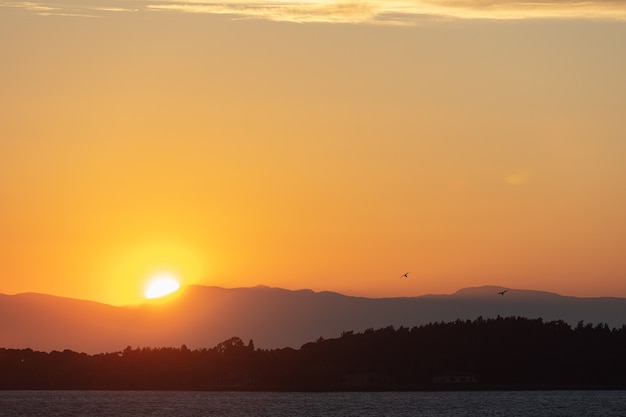 Paisagem dramática do nascer do sol em Urla, Izmir, Turquia. Paisagem deslumbrante do nascer do sol sobre o mar azul brilhante e o céu nublado laranja