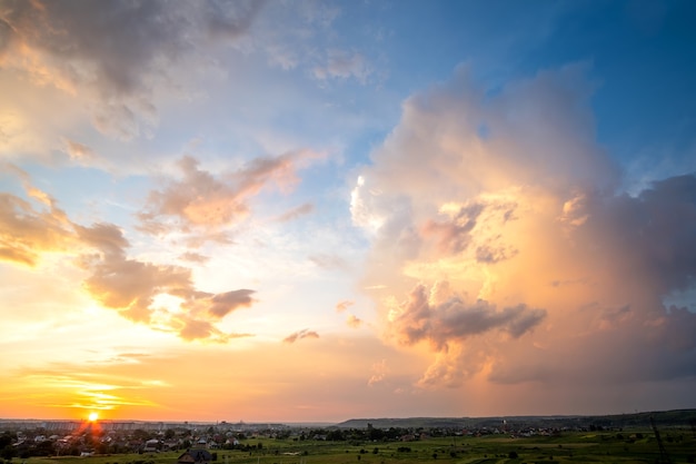 Paisagem dramática do sol da área rural com nuvens tempestuosas iluminadas pelo pôr do sol laranja e o céu azul.
