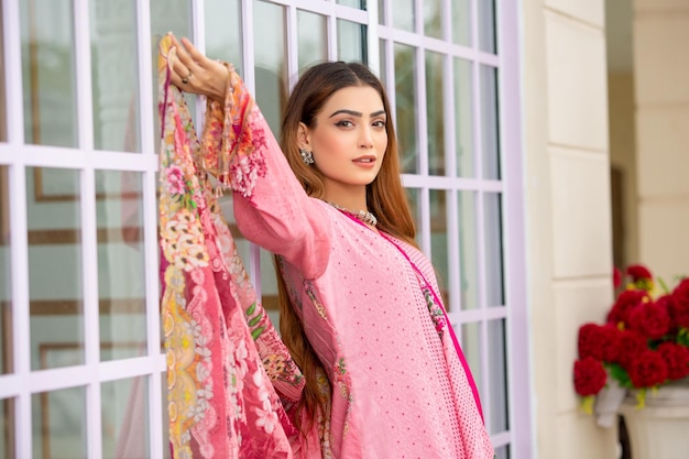 Paisagem jovem gostosa em pé com janelas e flores usando vestido Desi para sessão de fotos