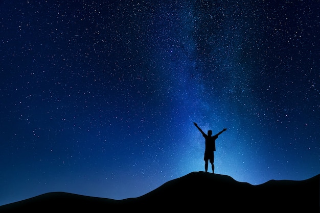 Paisagem linda noite da Via Láctea no céu nublado e a silhueta de um jovem com as mãos para cima.