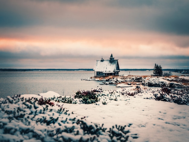 Paisagem minimalista do inverno nevado com uma autêntica casa de madeira ao entardecer na praia em uma aldeia russa de rabocheostrovsk. rússia.