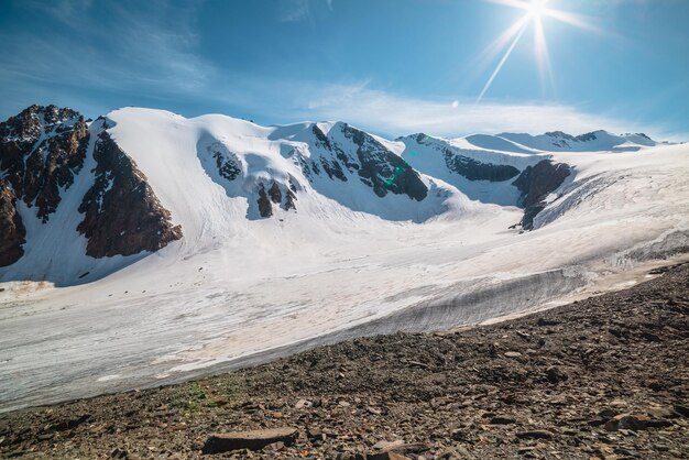 Paisagem montanhosa cênica com grande geleira à luz do sol Cenário incrível com língua glacial sob o sol no céu azul Bela vista alpina para nevar topos de montanhas em altitude muito alta em dia ensolarado