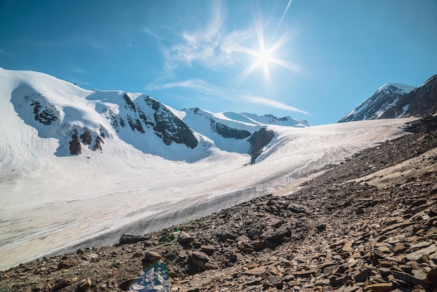 Foto paisagem montanhosa cênica com grande geleira à luz do sol paisagem incrível com língua glacial sob o sol no céu azul belas vistas alpinas para os picos de neve das montanhas em muito alta altitude em um dia ensolarado