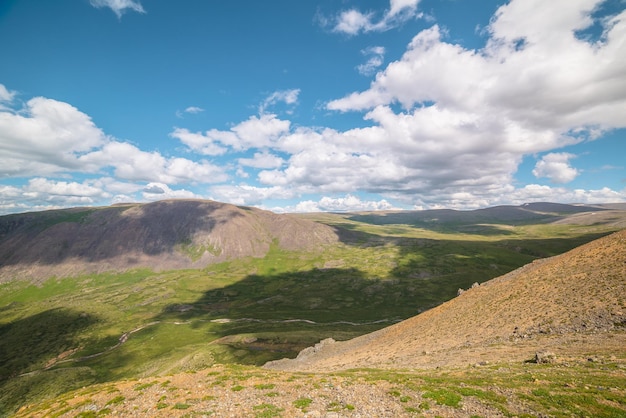 Paisagem montanhosa cênica com vale verde com rio e cordilheira com luz solar e sombras de nuvens em clima mutável Cenário alpino colorido com montanhas iluminadas pelo sol e céu nublado