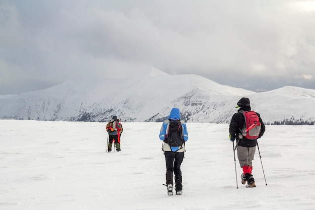 Paisagem montanhosa de inverno. três viajantes turistas caminhantes em roupas brilhantes com mochilas no campo nevado, caminhando em direção a uma montanha distante no fundo do espaço da cópia do céu nublado escuro azul tempestuoso.