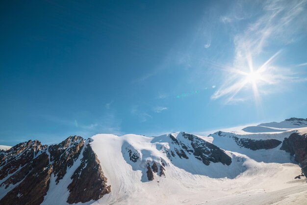Paisagem montanhosa minimalista com grande geleira à luz do sol Minimalismo nevado com língua glacial e sol no céu azul Vista alpina mínima para nevar o topo das montanhas em altitude muito elevada em dia ensolarado
