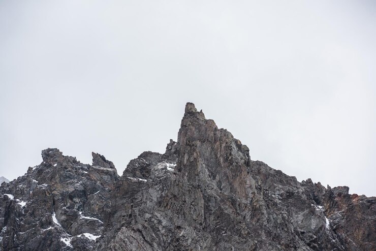 Foto paisagem montanhosa sombria com altas montanhas rochosas afiadas com neve no céu chuvoso cinza closeup de rochas afiadas e pico no céu nublado cinza cenário nublado sombrio com cordilheira com pico pontiagudo
