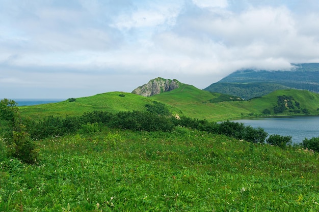 Paisagem natural da ilha de kunashir com vulcão de rochas vulcânicas de colinas gramíneas na lagoa de nuvens e oceano à distância