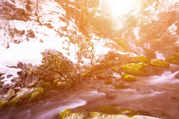 Paisagem natural incrível, bela cachoeira com luz solar na floresta de inverno profundo