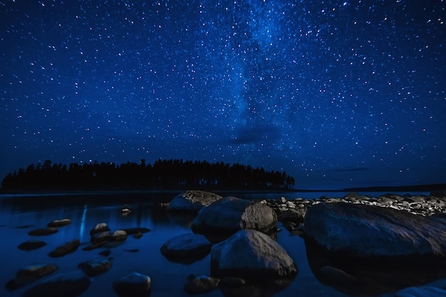 Paisagem noturna com céu estrelado sobre água do mar com pedras e floresta Astrofotografia com muitas estrelas Via Láctea